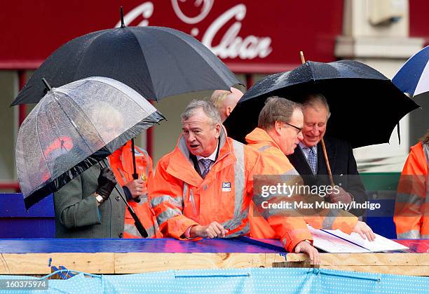 Camilla, Duchess of Cornwall and Prince Charles, Prince of Wales shelter under umbrellas as they view the Crossrail development site before...