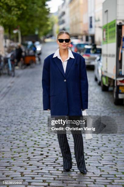 Tine Andrea wears blue striped oversized blazer, striped pants, white bag, button shirt outside Remain during the Copenhagen Fashion Week...