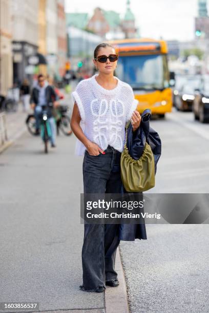 Darja Barannik wears navy coat, Loewe knit, grey denim jeans, green bag, sunglasses outside Remain during the Copenhagen Fashion Week Spring/Summer...