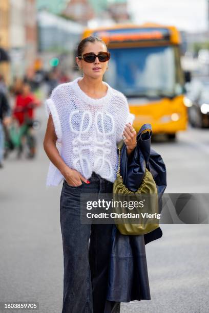 Darja Barannik wears navy coat, Loewe knit, grey denim jeans, green bag, sunglasses outside Remain during the Copenhagen Fashion Week Spring/Summer...