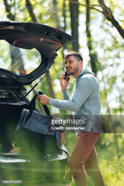 hübscher mann, der telefoniert, während er seine tasche aus dem auto nimmt - fachmann auto smartphone stock-fotos und bilder