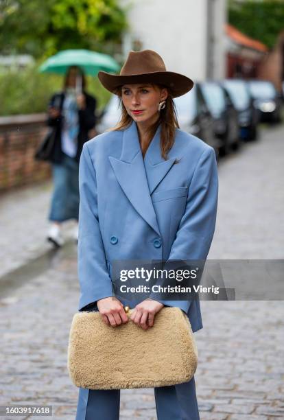 Guest wears brown cowboy hat, blue oversized blazer, teddy bag outside Skall Studio during the Copenhagen Fashion Week Spring/Summer 2024 on August...