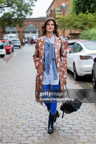 Guest wears coat with cow print, cowboy boots outside Skall Studio during the Copenhagen Fashion Week Spring/Summer 2024 on August 09, 2023 in...