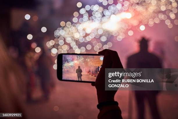 one person taking or filmimg a video of fireworks performance by her smartphone display in night sky on sparking background. horizontal photography. - movie explosion stockfoto's en -beelden