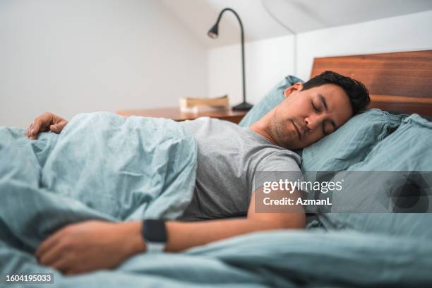 biracial man sleeping in bed with watch - sleep hygiene stock pictures, royalty-free photos & images