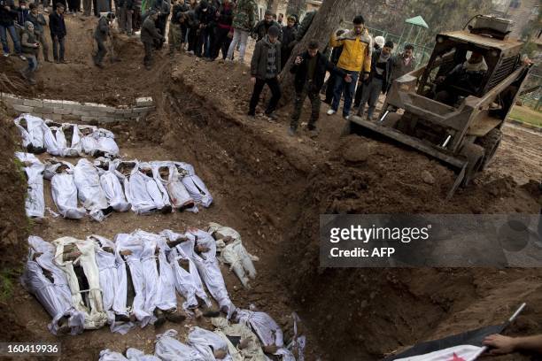 An earthmover pours soil on the bodies of Syrian civilians, who were executed and dumped in the Quweiq river, during their burial at a park now...