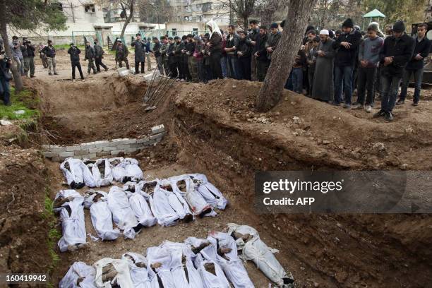 Syrian mourners pray over the bodies of civilians, who were executed and dumped in the Quweiq river, during their burial at a park now renamed...