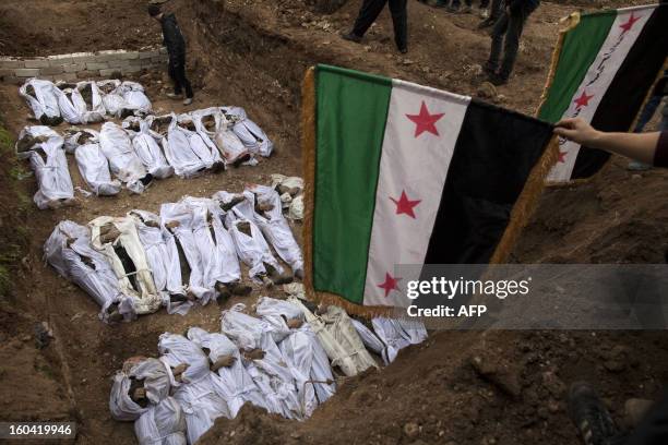 Syrian mourners wave the pre-Baath Syrian flag, now used by the Free Syrian Army, over the bodies of civilians, who were executed and dumped in the...