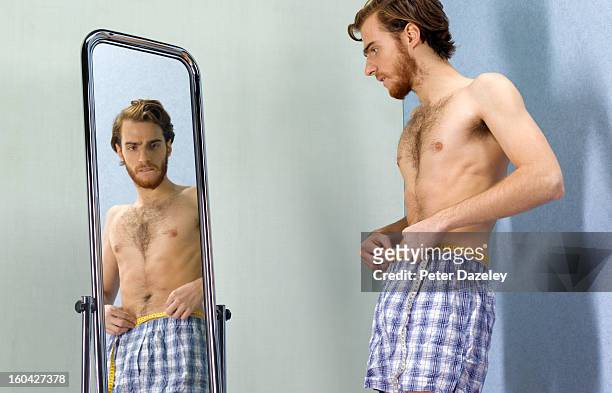 anorexic man looking worried into mirror - trastorno de alimentación fotografías e imágenes de stock