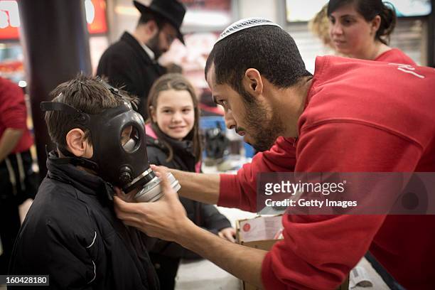Post office worker shows to an Israeli child how to wear a gas mask at a gas mask kit distribution station in a mall January 31 in Pisgat Ze'ev, East...