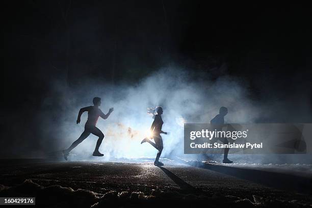 three runners on foggy road at night - dark background light stock-fotos und bilder