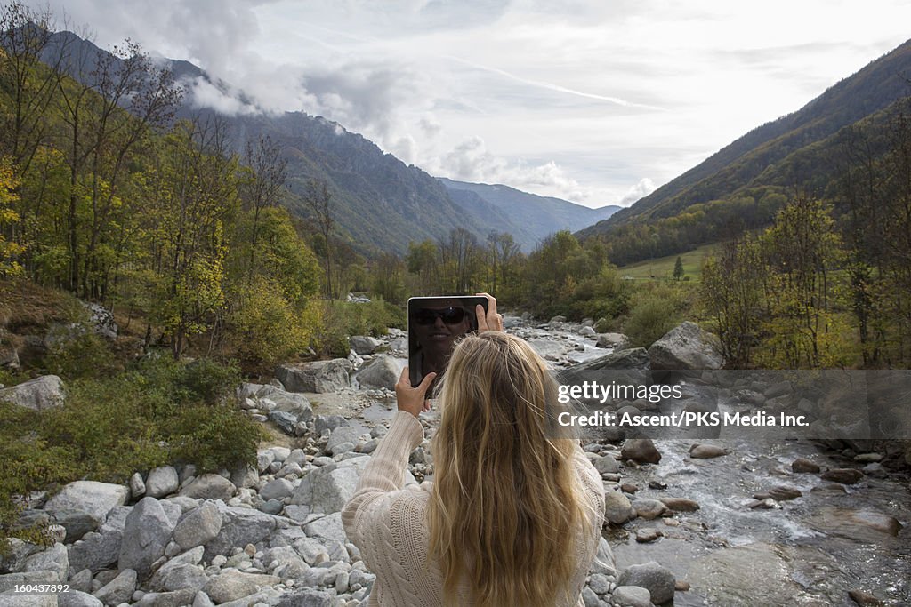 Woman taking a tablet photo from a mountain river