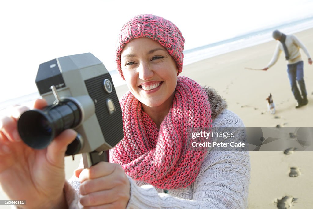 Woman filming on beach with man and dog