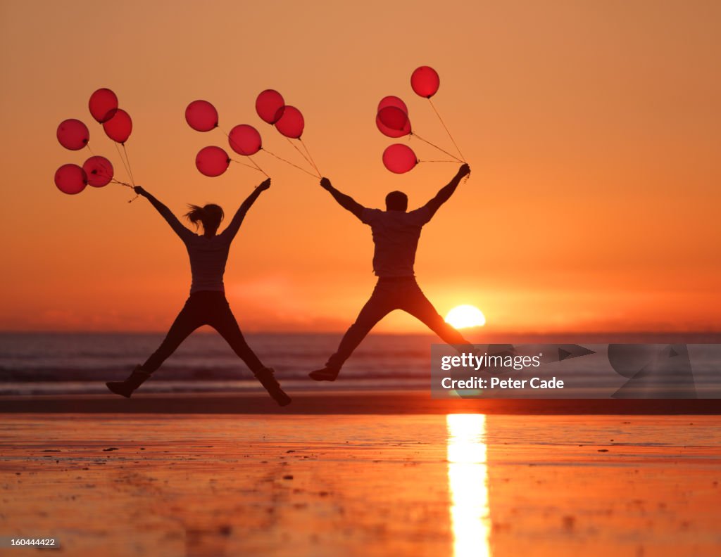 People jumping on beach at sunset holding balloons