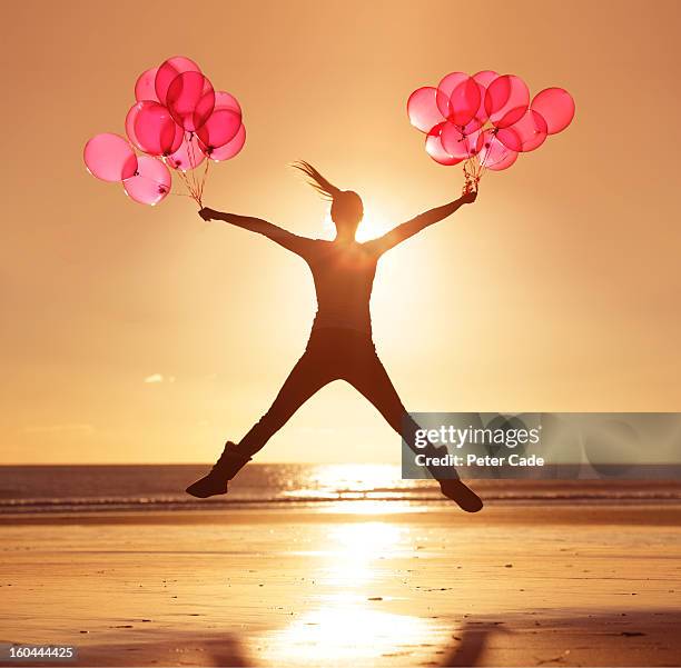 woman jumping on beach at sunset holding balloons - jumping jack stock pictures, royalty-free photos & images