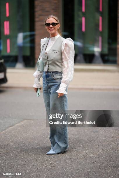 Guest wears black sunglasses, a white lace print pattern puffy shoulder pads / high neck blouse, a pale gray V-neck / sleeveless / buttoned gilet, a...