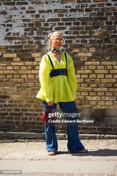 Guest wears gold sunglasses, gold earrings, a beige / brown / navy blue print pattern silk scarf as a large necklace, a yellow V-neck / long sleeves...