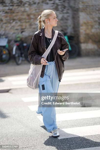 Guest wears a black tank-top from Adidas, a dar brown shiny leather bomber coat, pale blue large cargo pants from Adidas, a pale gray large crossbody...