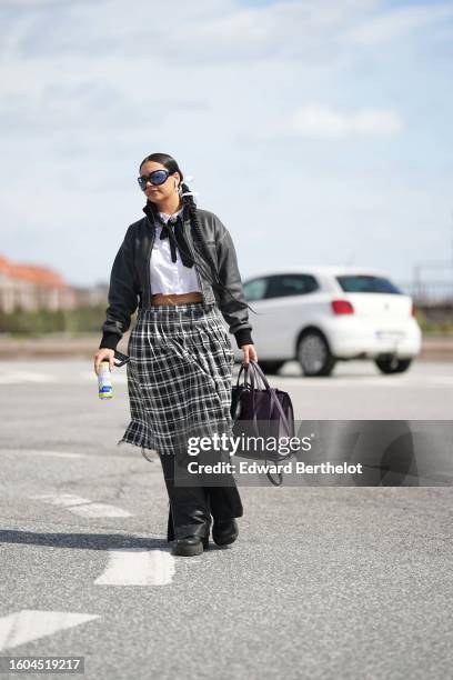 Guest wears black large butterfly sunglasses, silver earrings, a white shirt, a black silk knot bow-tie, a black shiny leather cropped jacket, a...
