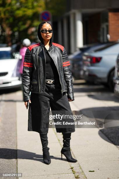 Guest wears black sunglasses, a black hoodie , a black t-shirt, a black shiny leather with red details pattern zipper biker jacket, a black shiny...