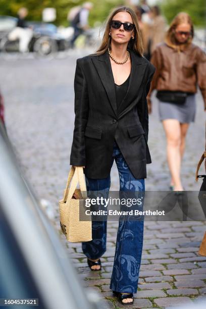 Guest wears black sunglasses, gold earrings, a gold pearls necklace, a black V-neck tank-top, a black shoulder pads blazer jacket, navy blue with...