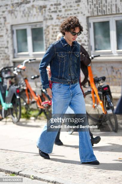 Guest wears black sunglasses, a navy blue denim jacket, pale blue faded denim flared pants, black shiny leather pointed block heels ankle boots ,...