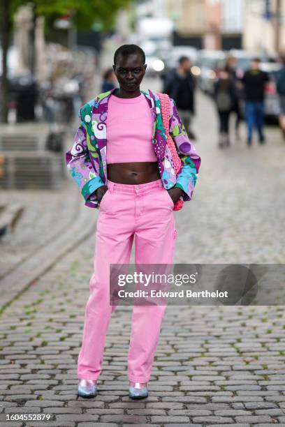 Guest wears a pink cropped t-shirt, matching pink suit pants, a purple / green / blue / white print pattern zipper jacket, a pink braided wool...
