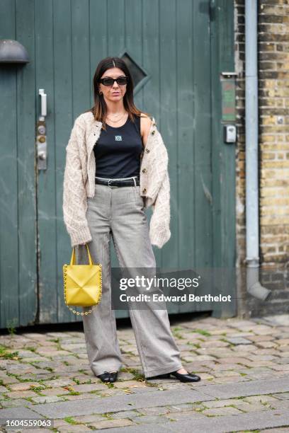 Guest wears black sunglasses, gold earrings, gold necklaces, a black tank-top from Loewe, a beige wool embossed checkered pattern buttoned cardigan,...