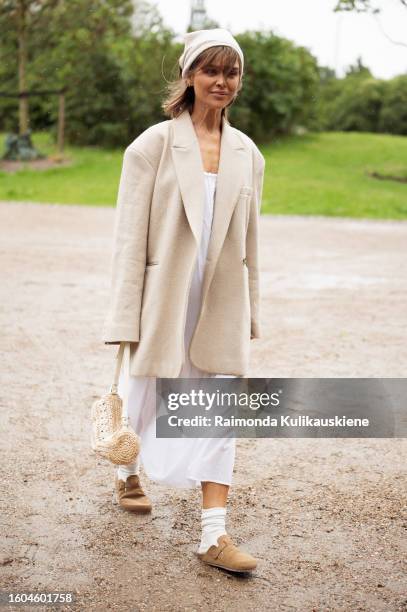 Gine Margrethe wears a white dress, beige oversized jacket, white socks, beige shoes, beige bag, and white head scarf outside OperaSport during the...