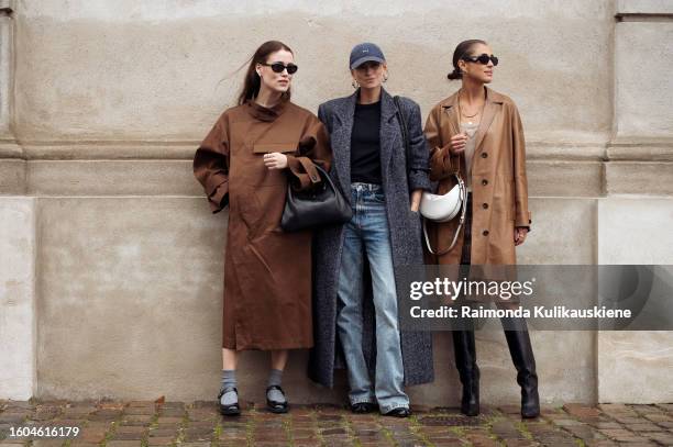 Annabel Rosendahl wears a brown coat, a black bag, and Tine Andrea wears a cap, a grey oversized coat, denim jeans, and Darja Barannik wears a brown...