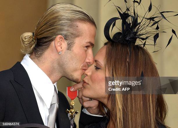 England football captain David Beckham kisses his wife, Victoria, as he holds the OBE he received 27 November 2003, from Britain's Queen Elizabeth II...