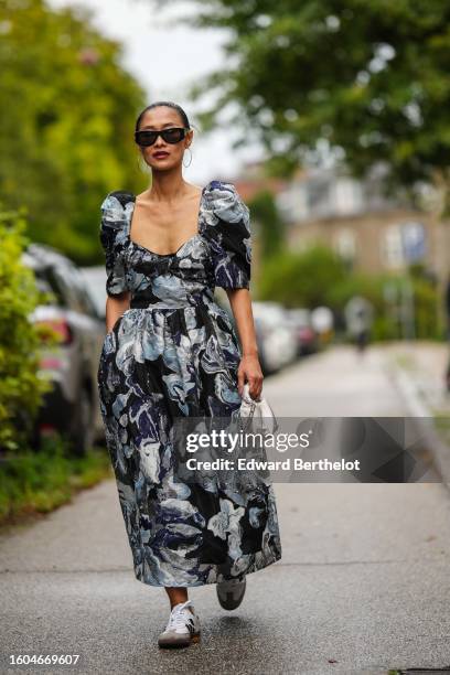Pornwika Spiecker wears black sunglasses from Loewe, a black with blue and silver flower large print pattern heart-neck / puffy short sleeves long...