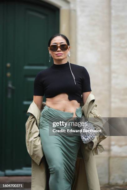 Miki Cheung wears brown squared sunglasses from Loewe, a black short sleeves / asymmetric cropped top, silver chain and rhinestones pendant earrings...