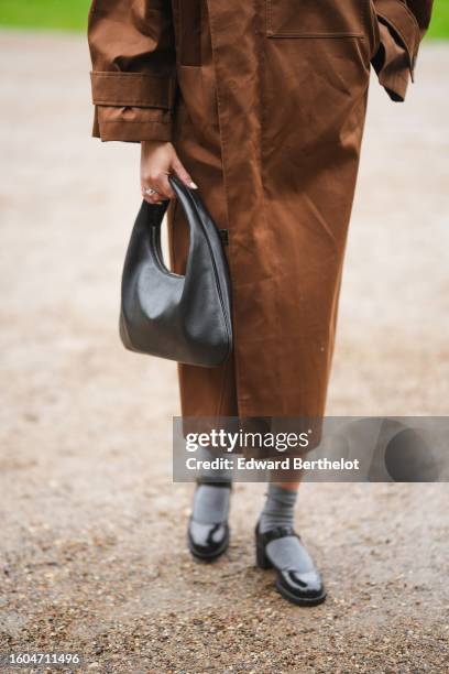 Annabel Rosendahl wears a dark brown high neck / flared long sleeves long coat, a black shiny leather handbag, gray socks, black shiny leather...