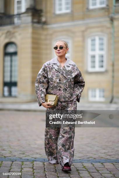 Justyna Czerniak wears black circle sunglasses, gold earrings, a pale gray with embroidered beige / purple / khaki embossed puffy flower pattern...