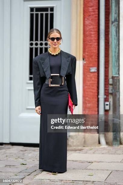 Nina Sandbech wears black futurist sunglasses, gold earrings, a large gold pearls necklace, a black cropped blazer jacket, a black long tube dress, a...