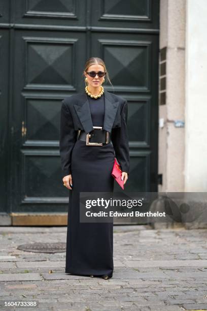 Nina Sandbech wears black futurist sunglasses, gold earrings, a large gold pearls necklace, a black cropped blazer jacket, a black long tube dress, a...