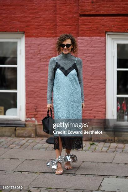 Renia Jaz wears black sunglasses, a gray wool turtleneck long sleeves t-shirt, a blue gray with black large borders V-neck / slit midi dress, a black...
