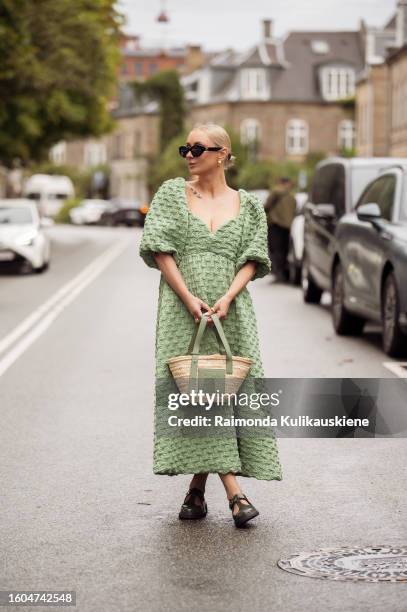 Justyna Czerniak wears black sunglasses, a green embossed pattern puffy short sleeves long dress, beige and green khaki Loewe, brown shiny leather...