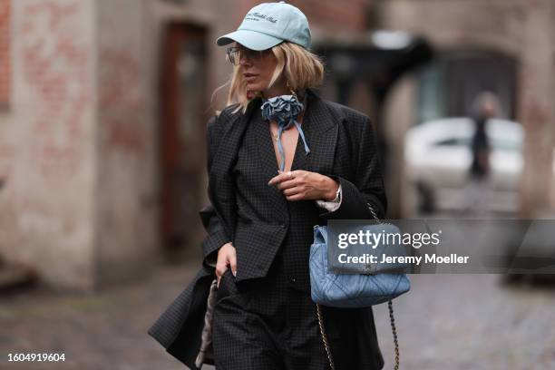 Karin Teigl seen wearing Munthe grey checked blazer jacket with matching suit pants, Sporty & Rich light blue cap, gold pendant earrings, Andy Wolf...