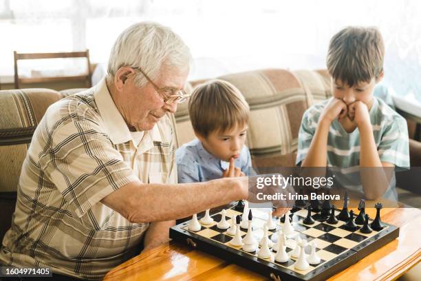 ein älterer grauhaariger mann bringt jungen das schachspielen bei. opa bringt seinen enkelkindern das schachspielen bei. - compassionate eye stock-fotos und bilder