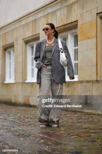 Guest wears black sunglasses, white pearls earrings, a white large pearls necklace, a gold necklace, a pale gray striped print pattern blazer jacket,...