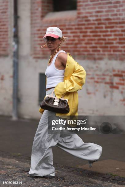 Karin Teigl seen wearing Andy Wolf light blue transparent pilot sunglasses, red / white baseball cap, gold earrings and statement chain necklace,...
