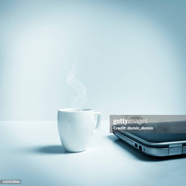 closed laptop with mug of hot tea, coffee, blue toned - white coffee cup stock pictures, royalty-free photos & images