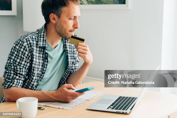 male paying with debit card while doing shopping on internet on laptop - phishing fotografías e imágenes de stock