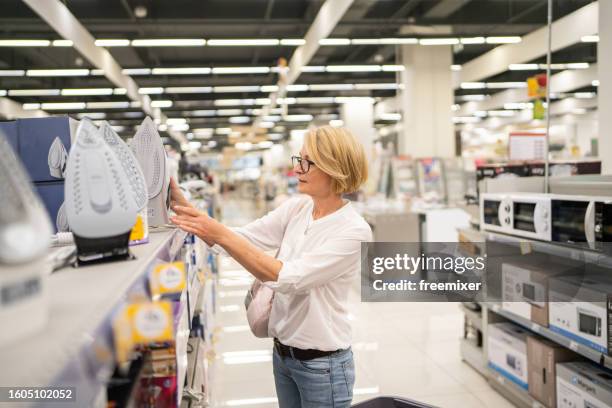 mature woman in appliance store - iron appliance stockfoto's en -beelden