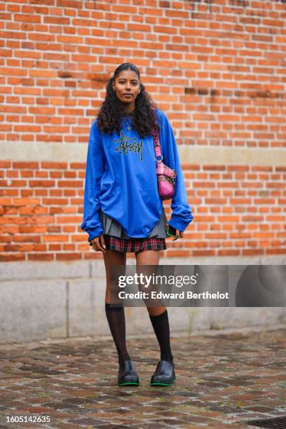 Guest wears a gold chain with sun pendant necklace, a royal blue with black inscription pattern sweater, a beige and brown monogram print pattern...