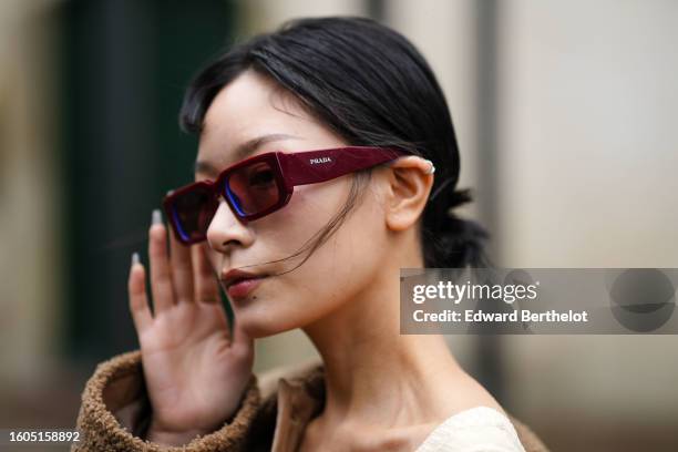Guest wears burgundy squared sunglasses from Prada, a beige heart-neck / cut-out chest / short tube jumpsuit, a brown shiny leather and sheep fur...