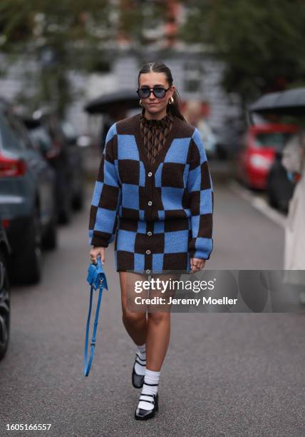 Lina Uhrig seen wearing Corlin Eyewear black sunglasses with blue transparent lenses, gold earrings, Gestuz brown / black triangle print pattern...