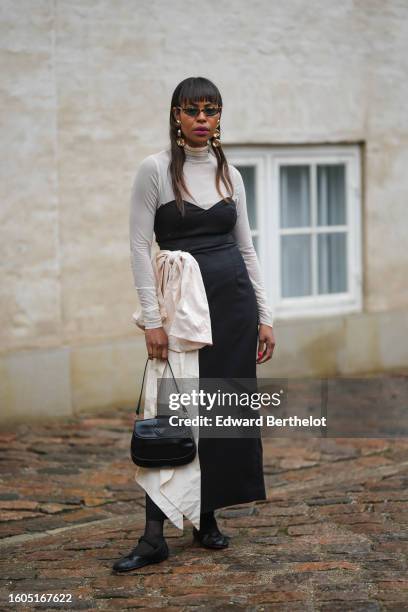 Guest wears black and yellow marble print pattern sunglasses, gold large earrings, a white latte tulle turtleneck long sleeves t-shirt, a black...